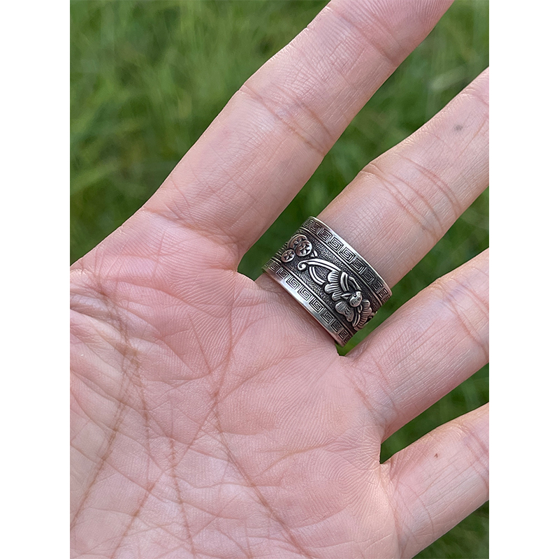 Lion Rolling Ball Engraved Silver Ring The "Lion Rolling an Embroidered Ball" is a classic auspicious pattern: the lion symbolizes majesty and protection, warding off evil and misfortune. The ball is no ordinary toy, it was a variation of the ancient Chinese saying "Taiping Youxiang" (meaning "peaceful and prosperous") or a "lucky object." Its rolling motion symbolizes "good fortune is coming," and the overall pattern conveys the auspicious wish of "warding off disasters, welcoming blessings, a smooth life, and prosperity and good fortune." The curling ring pictured above is made of S990 fine silver, weighing approximately 9.4g and measuring approximately 17.4mm wide. This vintage silver curling ring features a core craftsmanship element: the "rolling" element. Through hammering, curling, and shaping the silver, a smooth, linear texture is achieved. Combined with the three-dimensional engraving of the "Lion Rolling an Embroidered Ball," the lion's mane and the texture of the ball are distinctly layered. The ring combines the matte finish of vintage silver jewelry with the refined details of traditional patterns, embodying the fusion of traditional metal forging and engraving techniques.