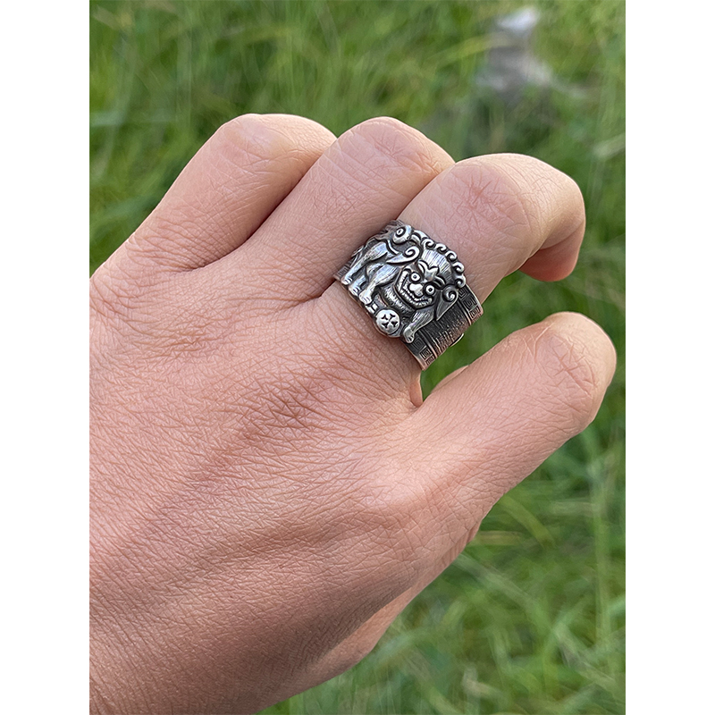 Lion Rolling Ball Engraved Silver Ring The "Lion Rolling an Embroidered Ball" is a classic auspicious pattern: the lion symbolizes majesty and protection, warding off evil and misfortune. The ball is no ordinary toy, it was a variation of the ancient Chinese saying "Taiping Youxiang" (meaning "peaceful and prosperous") or a "lucky object." Its rolling motion symbolizes "good fortune is coming," and the overall pattern conveys the auspicious wish of "warding off disasters, welcoming blessings, a smooth life, and prosperity and good fortune." The curling ring pictured above is made of S990 fine silver, weighing approximately 9.4g and measuring approximately 17.4mm wide. This vintage silver curling ring features a core craftsmanship element: the "rolling" element. Through hammering, curling, and shaping the silver, a smooth, linear texture is achieved. Combined with the three-dimensional engraving of the "Lion Rolling an Embroidered Ball," the lion's mane and the texture of the ball are distinctly layered. The ring combines the matte finish of vintage silver jewelry with the refined details of traditional patterns, embodying the fusion of traditional metal forging and engraving techniques.